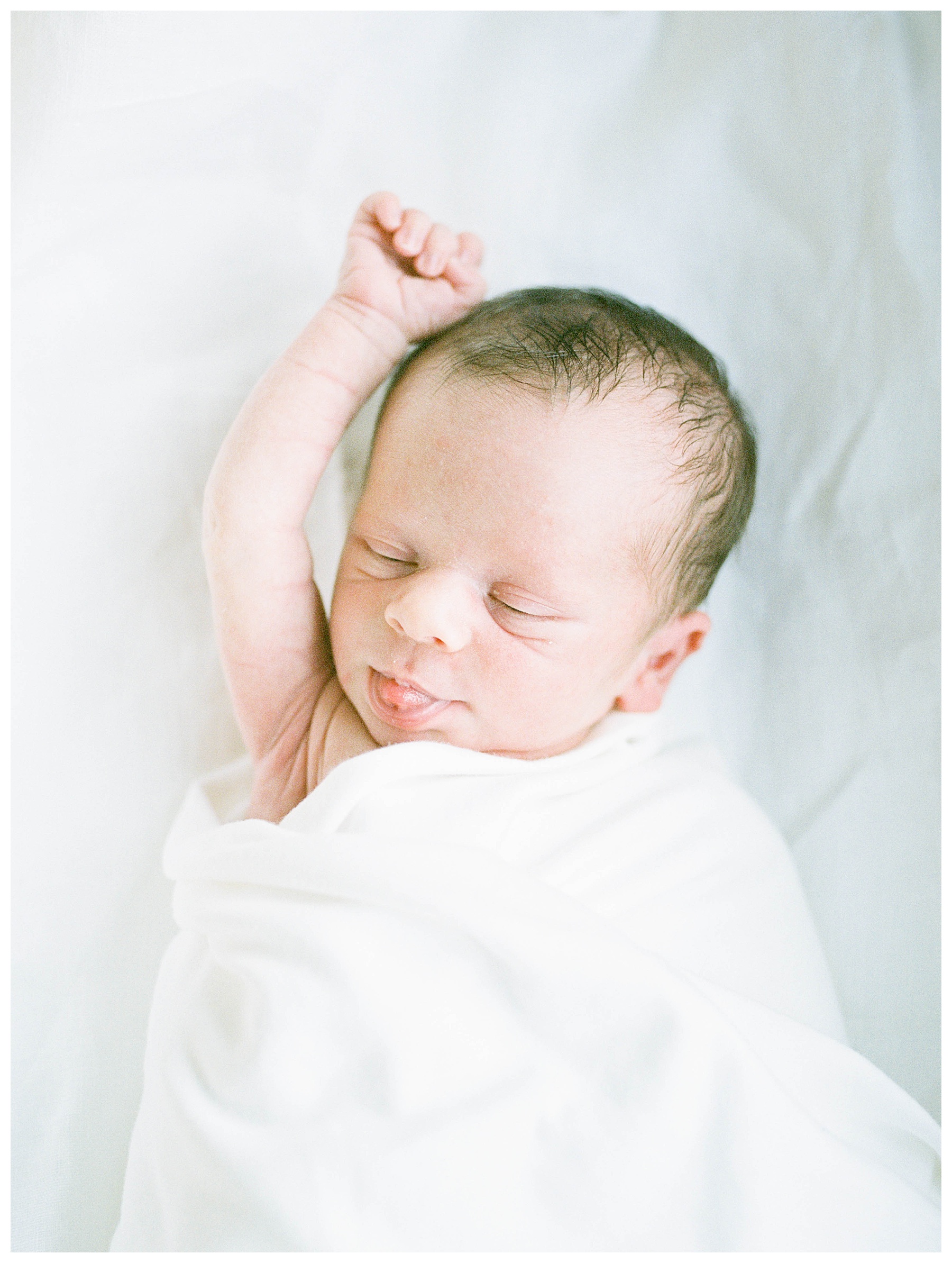 newborn baby with right arm raised over his head